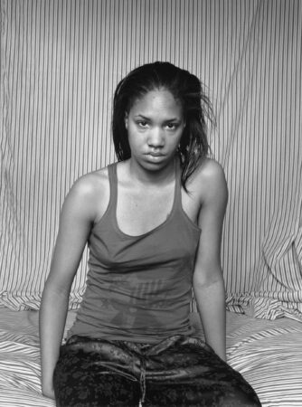 Black and white self portrait of the artist LaToya Ruby Frazier in front of a striped fabric background. 
